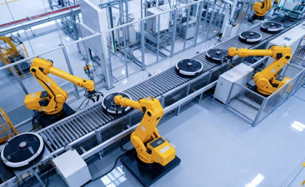 Yellow industrial robotic arms collaborating on an automated assembly line in a smart factory, handling robot vacuum cleaners on a roller conveyor